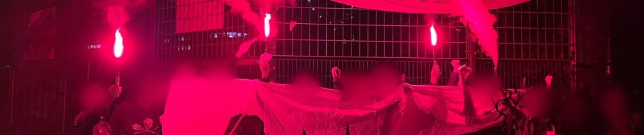 Gruppe aktivistischer Menschen bei Nacht mit roter Pyro. Auf den Transpis steht: Unser Görli bleibt offen!